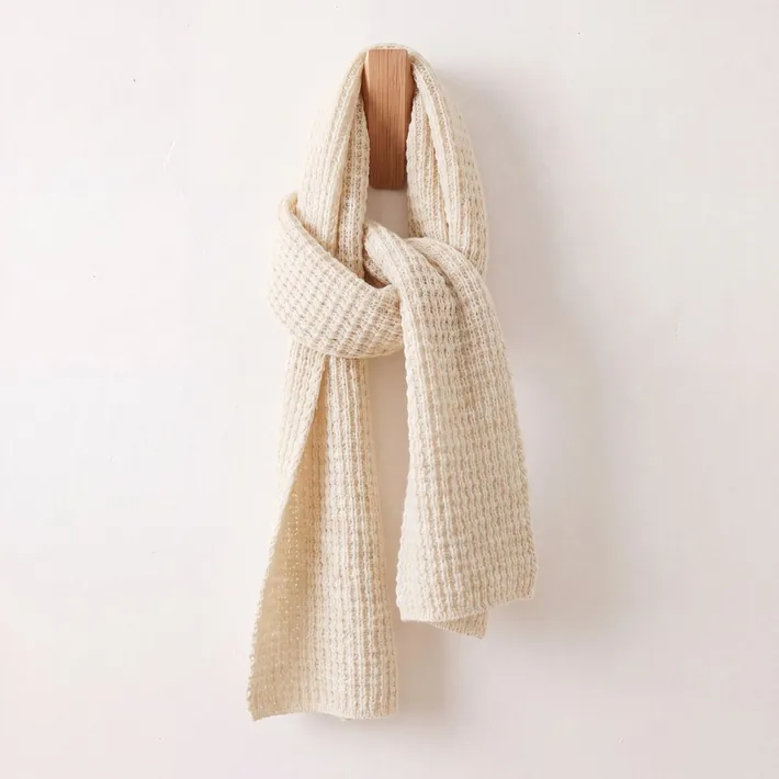 Cream waffle knit baby alpaca scarf displayed on a wooden wall hook