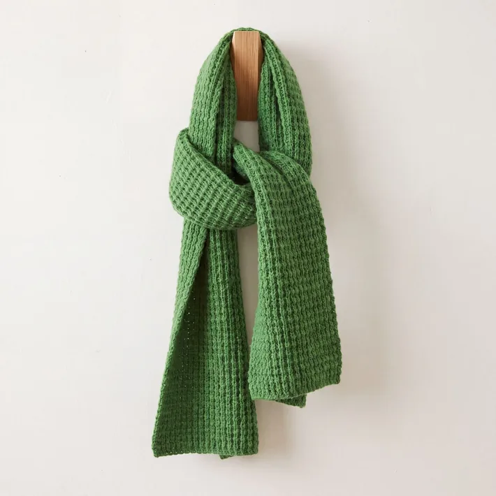 Green waffle knit baby alpaca scarf displayed on a wooden wall hook