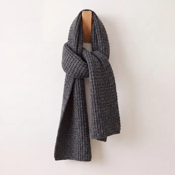 Charcoal grey waffle knit baby alpaca scarf displayed on a wooden wall hook
