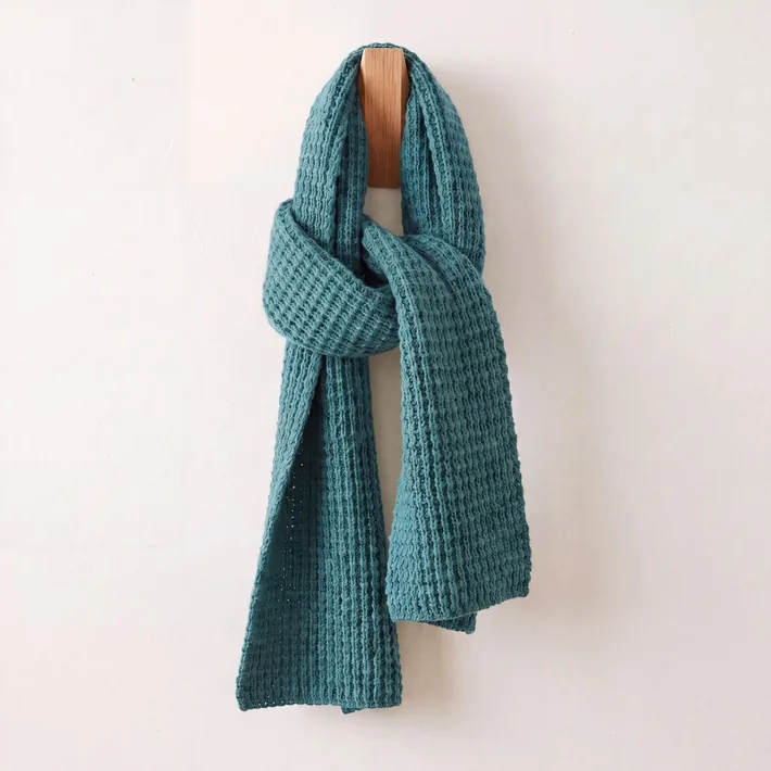 Teal waffle knit baby alpaca scarf displayed on a wooden wall hook