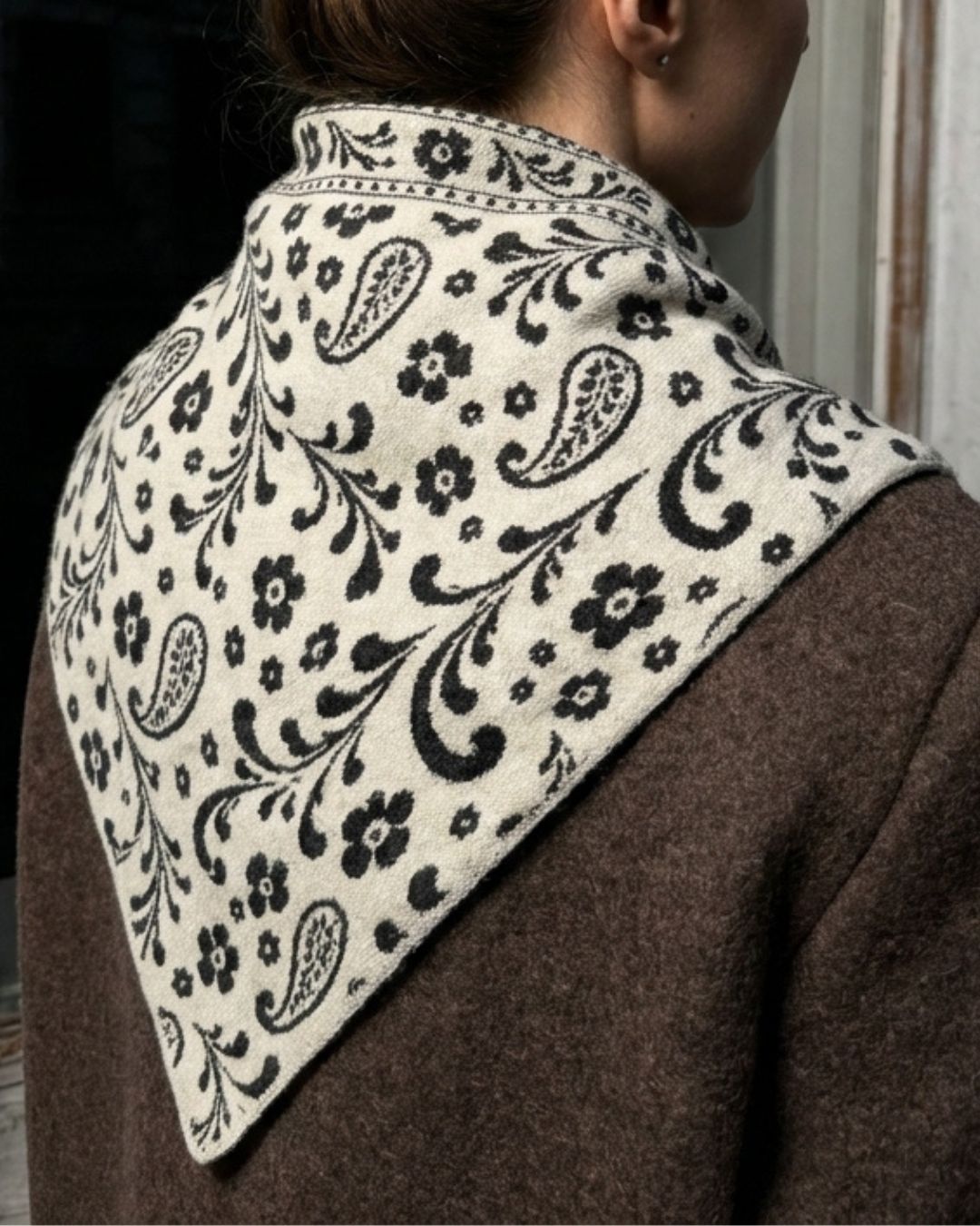 Model wearing the grey and white reversible paisley alpaca triangle scarf in a bookshop